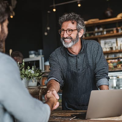 Local Business Owner Funded by Impelly Financial - Success Story Small business owner smiling and shaking hands with funding partner inside a coffee shop after receiving capital from Impelly Financial